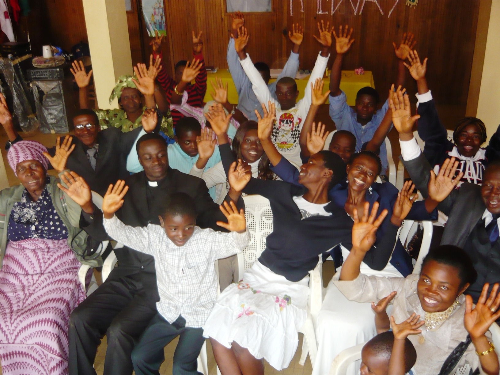 Community members gathered indoors, smiling with raised hands