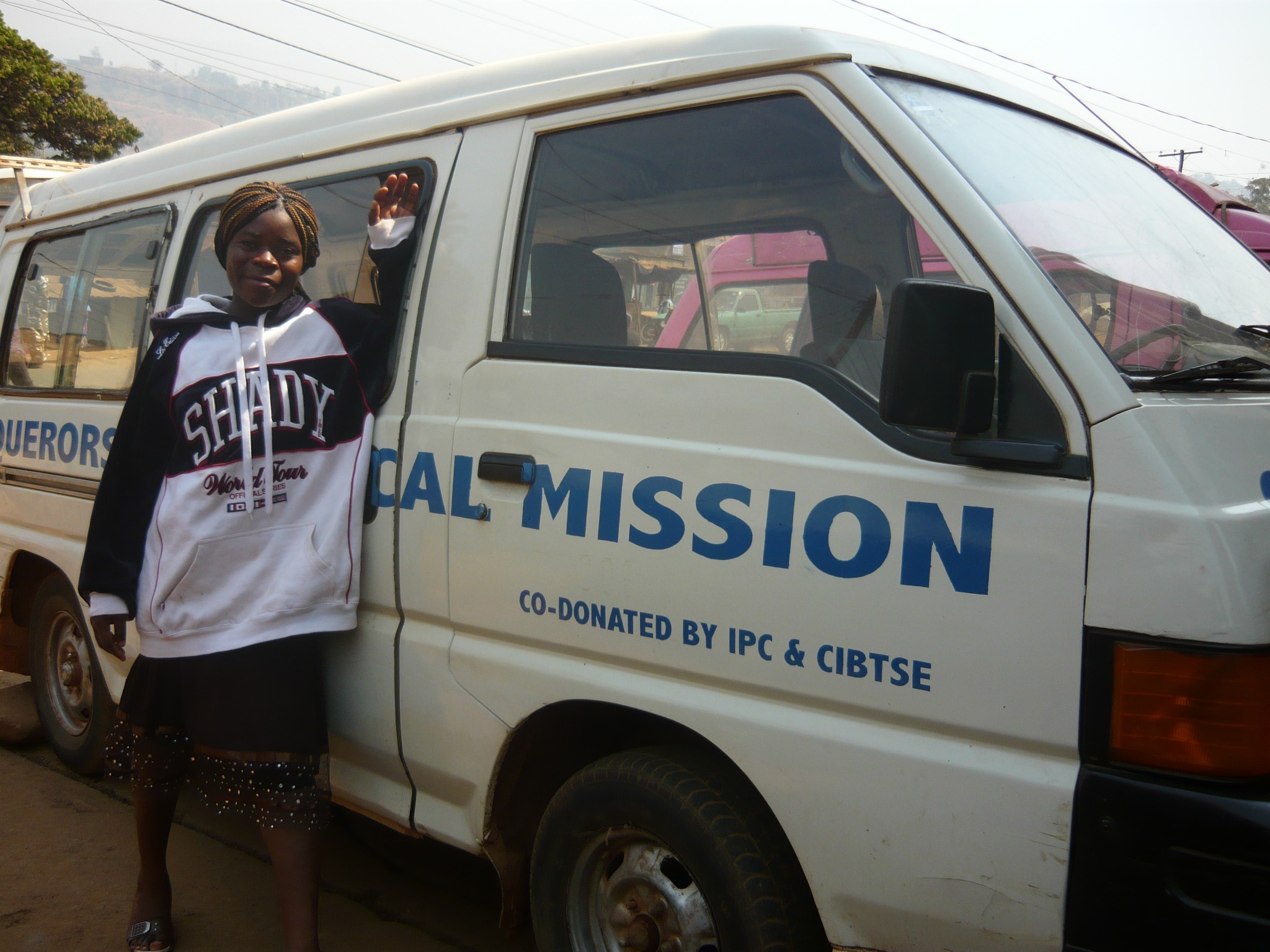 Person standing beside a white Conquerors Evangelical Mission van